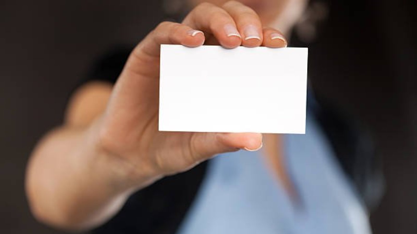 Close-up of a blank business card in businesswoman's hand. Dark background. You can put your text.